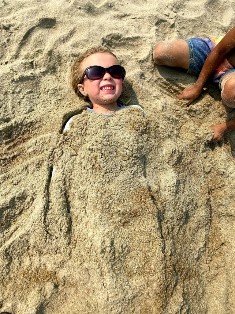 A smiling child buried in sand embodies carefree calm — joyful rest beside a hidden coastal sanctuary along Riviera Nayarit’s shore.