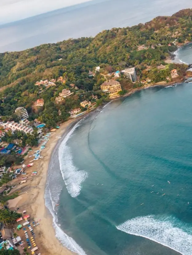 Soft waves shimmer near fishing boats and surfers at Playa Sayulita — a boutique coastal retreat alive with sunlight and calm.