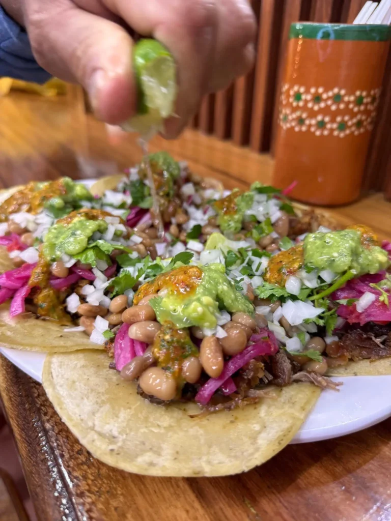 A hand squeezes lime over tacos with salsa and cilantro — a Sayulita getaway moment celebrating fresh street flavor and coastal simplicity.