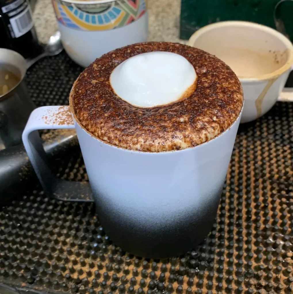 Un mocha recién preparado muestra espuma espolvoreada con chocolate y un suave toque de leche vaporizada, transmitiendo la riqueza tipo postre de este mocha.