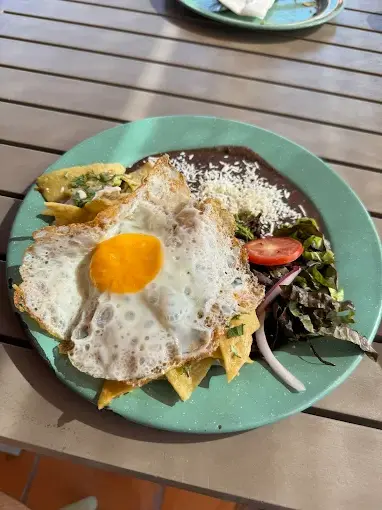 Crispy chilaquiles topped with a sunny-side egg, refried beans, and fresh greens create a vibrant breakfast served on the terrace at Casa Paraíso