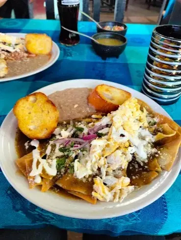 A hearty plate of chilaquiles topped with crema, cheese, onions, and herbs, served with beans and toasted bread at a local Sayulita breakfast spot.