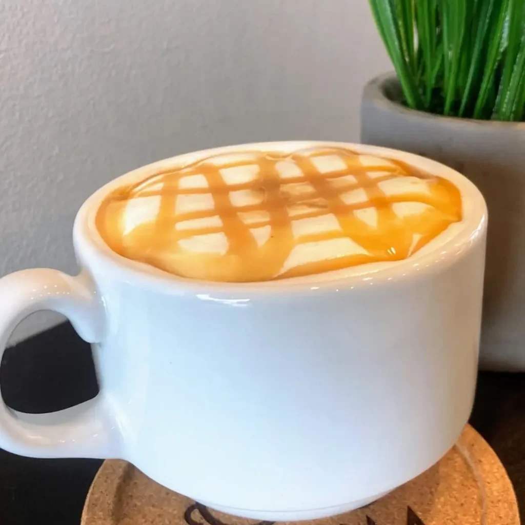 Un macchiato recién hecho se cubre con espuma sedosa y un toque de caramelo, mostrando la combinación de espresso intenso y dulzura ligera.
