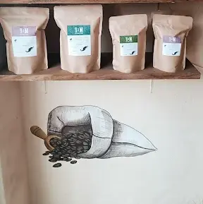 Bolsas de café recién tostado llenan el estante en M&F Coffee Roasters sobre un mural de granos derramándose que muestra la artesanía de este café de Sayulita.