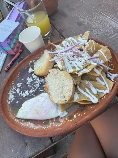 Crisp chilaquiles topped with crema, cheese, and red onion sit beside refried beans and a fried egg, creating a filling breakfast at Northside Café