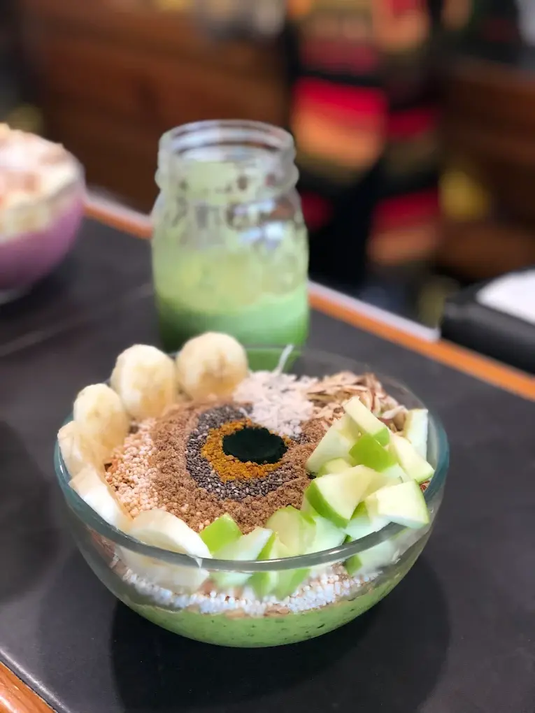 A superfood bowl with banana, green apple, seeds, and coconut sits beside fresh green juice, creating a colorful and energizing breakfast at Orangy