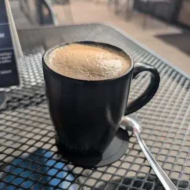 Un café caliente recién preparado descansa sobre una mesa en el patio de YAH-YAH Café, capturando un tranquilo momento matutino y el sabor intenso de este favorito de Sayulita.
