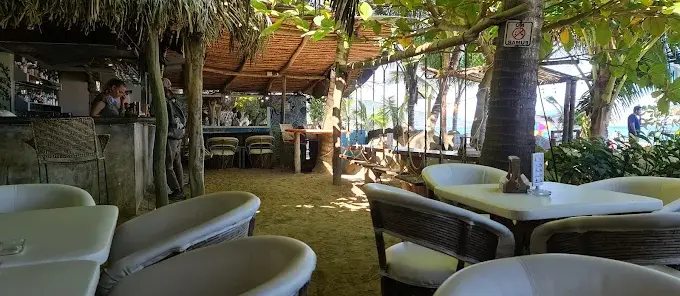 Relaxed sand-floor seating at Bar La Isla with a shaded palapa roof, beachfront bar, and casual tables, creating a laid-back seafood and tropical cocktail atmosphere.