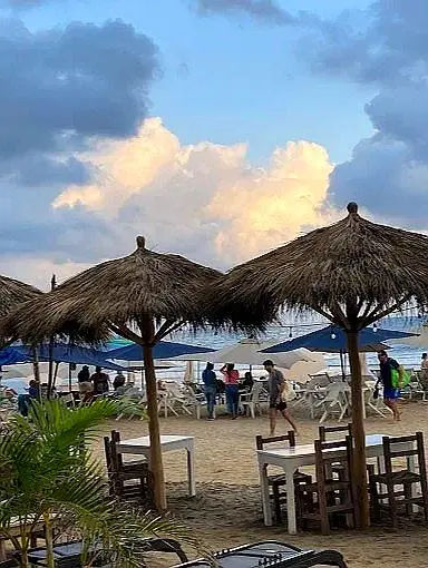 Palm umbrellas cast soft shadows as the sun settles over Sayulita’s shoreline, warming the sky along Mexico’s Western Riviera Coast during a calm evening.