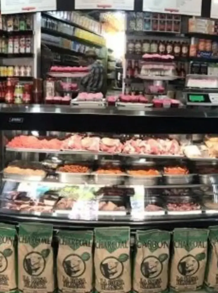 A butcher counter filled with trays of fresh meat sits below shelves stocked with sauces, seasonings, and pantry items, creating a well-supplied shop.