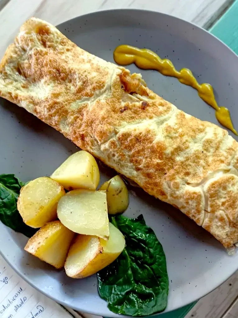 A warm breakfast wrap served with golden potatoes and greens creates a hearty, comforting morning plate at Chaman, a tranquil garden café in Sayulita