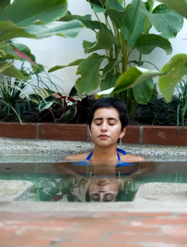 Woman in cold plunge surrounded by tropical flora—rejuvenating contrast therapy within a magical garden designed for calm recovery.
