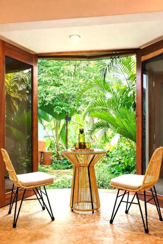 Dining nook with woven chairs, sculptural table, and open doors to a quiet courtyard—an easy start to the day at Amari’s seaside retreat.