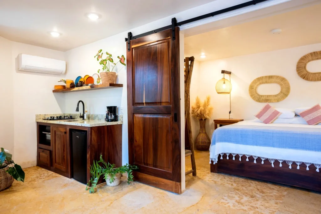 Cove Suite 2 overview with full kitchen, sink, mini fridge, and coffee station, with handcrafted doors leading into the bedroom area at Amari Hotel.