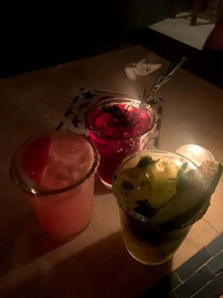 Three creative margaritas on a dim bar table in Sayulita, featuring salted rims, fruit garnishes, and candlelight at a bar known for unique flavors.