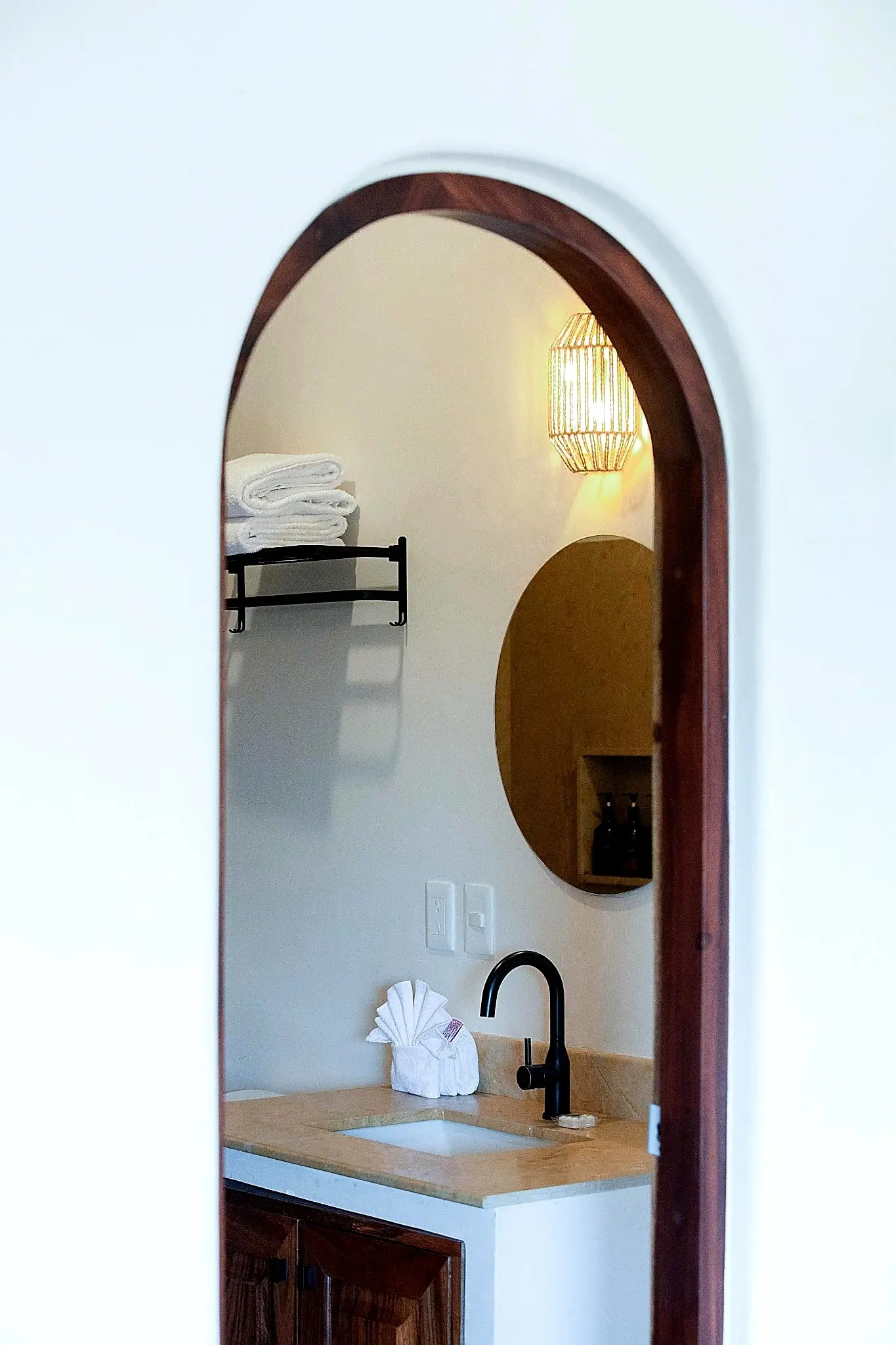 Bathroom Vanity With Arched Doorway, Round Mirror, and Black Faucet