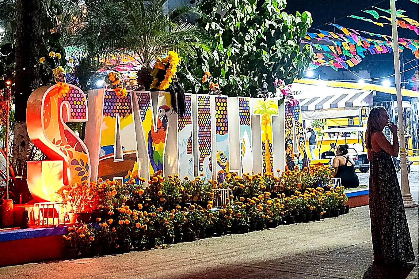 “Sayulita” letters glowing at night in the town plaza, with marigolds and festive flags—an iconic evening scene near Amari.