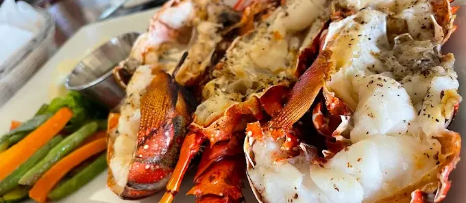 Grilled lobster at Don Pedro’s with sautéed vegetables and seasoned butter, known for refined beachfront seafood and a classic coastal dining style.