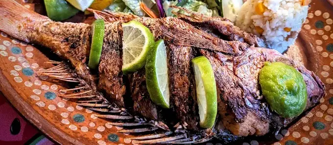 Whole grilled fish at El Jakal with lime, salsa, rice, and salad on a traditional Mexican plate, known for classic mariscos and familiar local flavors.