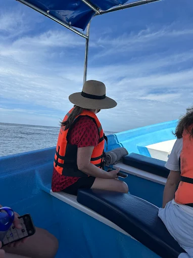 A person wearing a life jacket watches the water from a boat near the Nayarit Coast while observing wildlife nearby.
