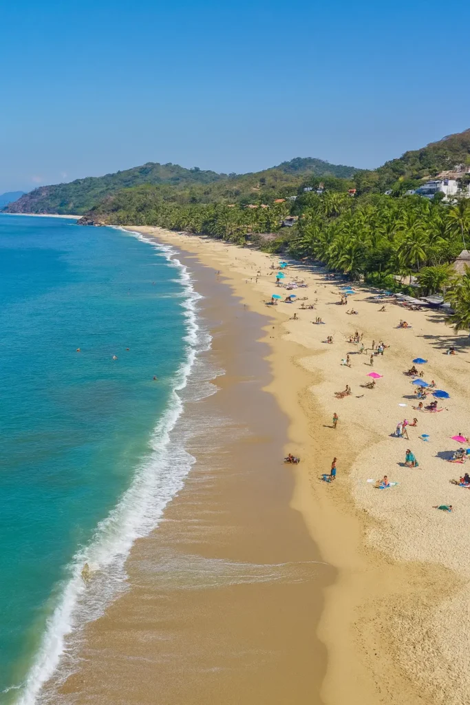 Families relax under umbrellas as children splash in gentle surf—a safe stretch of golden sand on the Pacific Riviera ideal for peaceful family days.