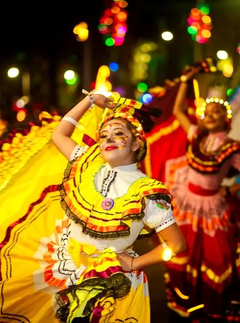 A folklórico dancer twirls in bright yellow skirts beneath festival lights, celebrating Mexico’s cultural heritage during a joyful nighttime parade.
