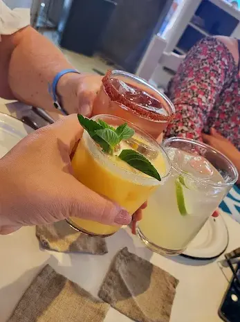 Friends toasting with colorful cocktails in Sayulita, including a mint-topped tropical drink, a classic lime margarita, and a chili-rimmed beverage.