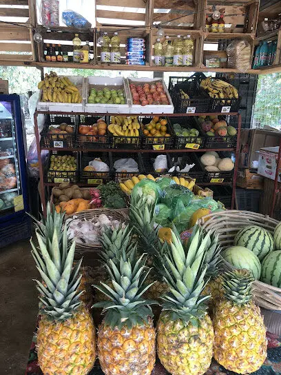 Pineapples, watermelon, bananas, apples, citrus, and other fruits arranged in baskets and crates inside a produce shop with fully stocked shelves.