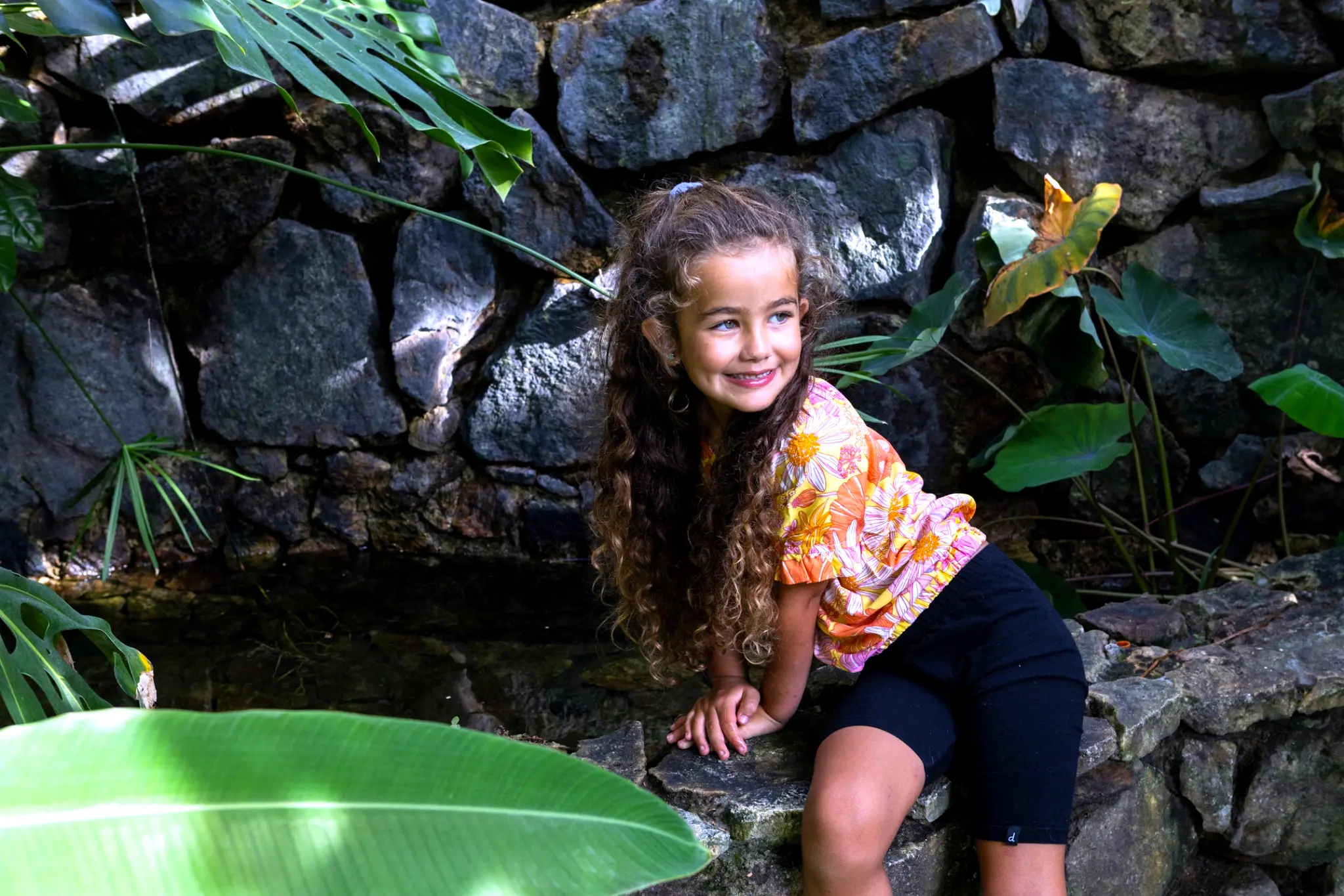 Child enjoying a tropical garden waterfall and pond surrounded by lush greenery, creating a calm hideaway for family-friendly relaxation and play.