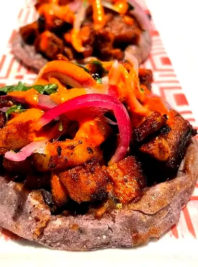 Handmade sopes topped with pork, beans, pickled onions, and salsa, highlighting thick masa, savory toppings, and bold flavor in Mexican street snacks.