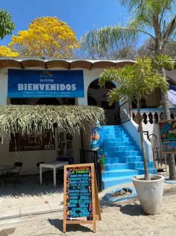 Entrance of La Panga Seafood & Grill with a bright blue staircase, shaded outdoor seating, and a colorful sign for grilled pescado zarandeado and family recipes.