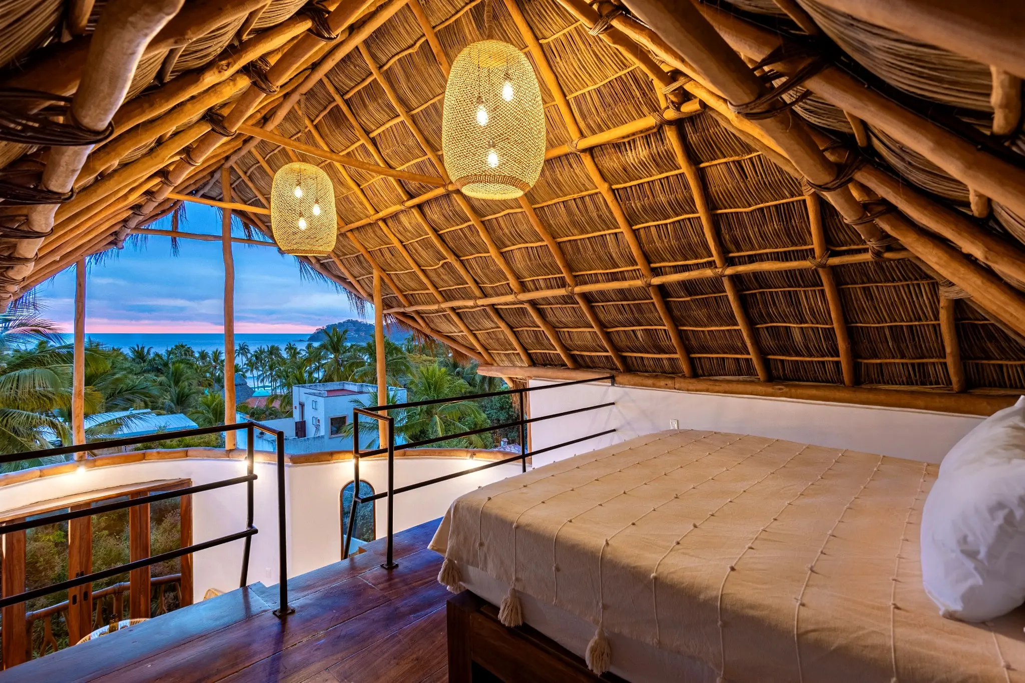 Serene loft bedroom beneath a handcrafted palapa roof, opening to ocean views and sunset skies for an elevated, calming sleep experience.
