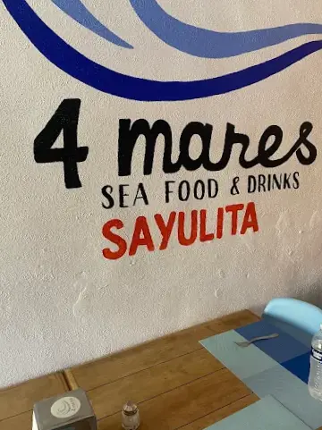 Wall sign inside 4 Mares Seafood & Drinks above a wooden table setting, representing the restaurant’s casual, family-run atmosphere and generous mariscos plates.