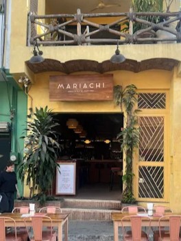 Outdoor seating at a Sayulita bar named “Mariachi,” featuring a yellow facade, wood signage, and tables along the street for guests to enjoy drinks.