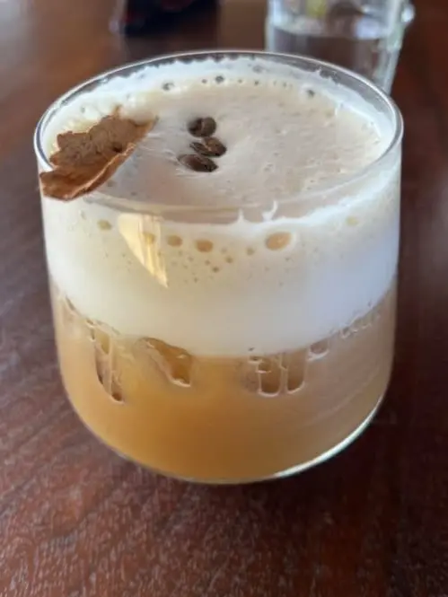Mezcal carajillo served over ice with a creamy foam layer, coffee beans, and a dried garnish, offered as an after-dinner cocktail in Sayulita.