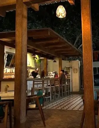 Open-air bar in Sayulita at night with wooden seating, pendant lighting, and two guests at the counter enjoying signature cocktails.