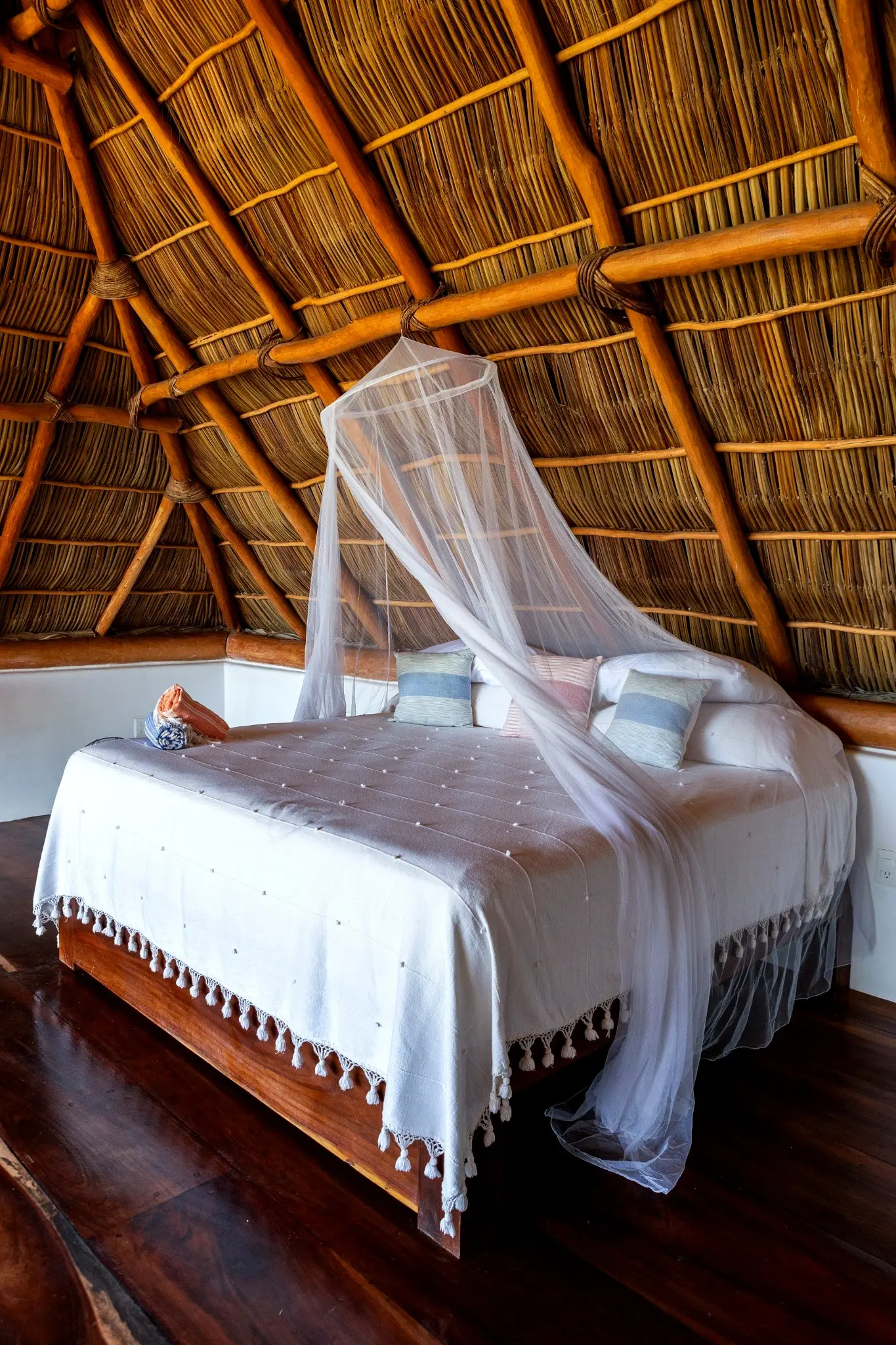 Lofted King Bed With Mosquito Netting Beneath a Thatched Ceiling