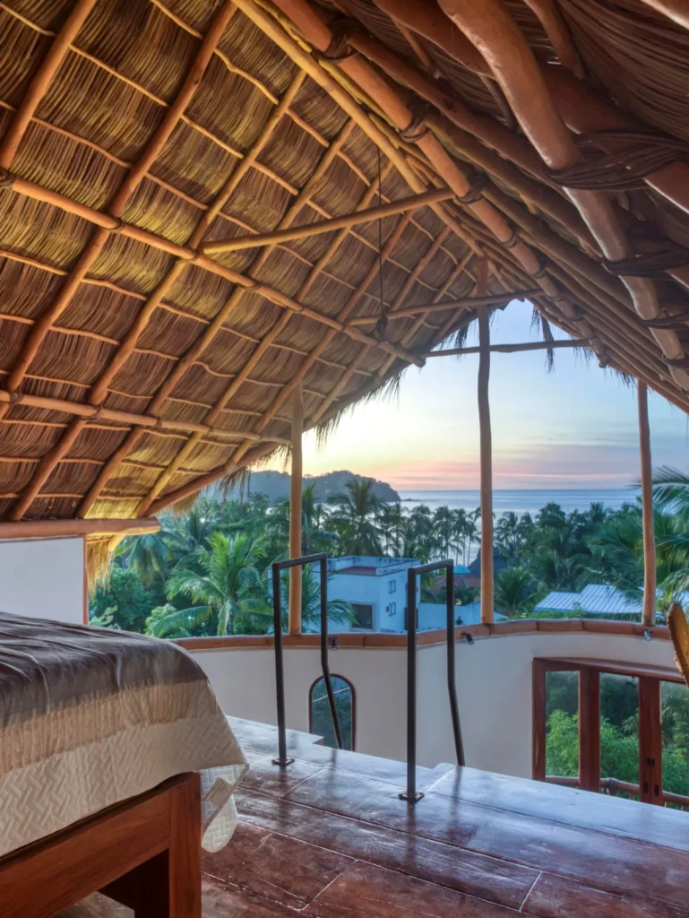 Open-air loft bedroom at Amari Boutique Hotel with palm-lined views and natural textures, offering a peaceful setting overlooking the Pacific coastline of Sayulita at dawn.