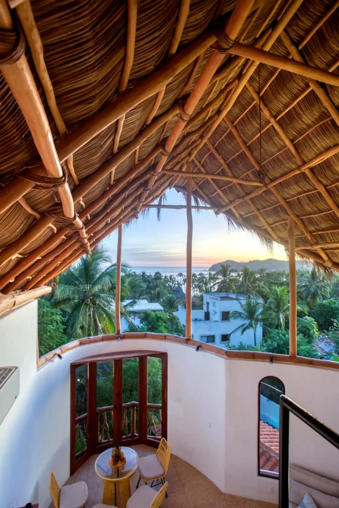 Sunrise view from Amari’s palapa rooftop loft with bamboo ceiling, arched doors, and ocean horizon above palms—peaceful mornings in Riviera Nayarit.