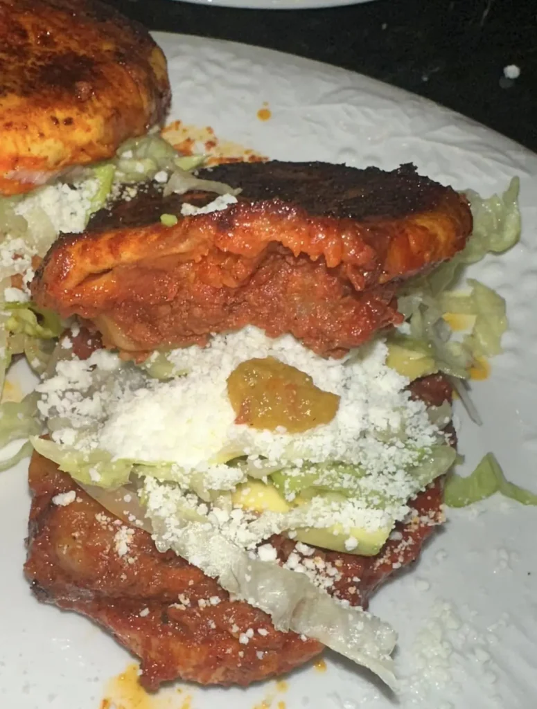 Pambazo dipped in red chile sauce and filled with potatoes, chorizo, lettuce, and cheese, highlighting spicy sauce, soft bread, and hearty flavor.