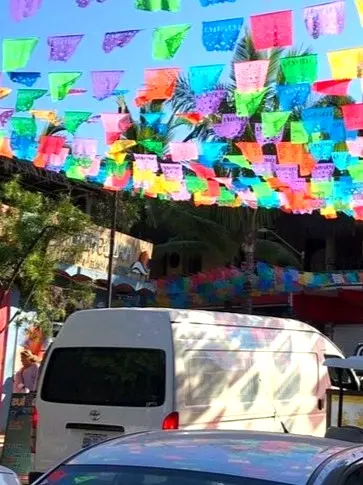 Colorful papel picado banners flutter over Sayulita’s plaza as vendors chat and guitars play, framing the village’s vibrant Pacific coast culture.