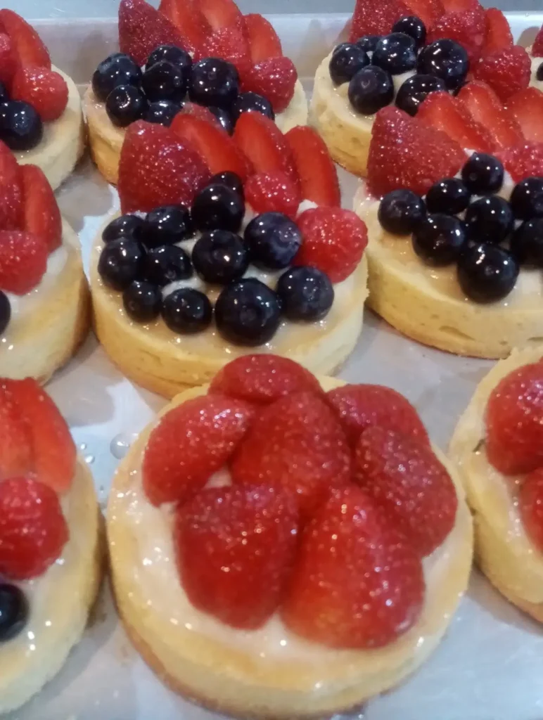 Mini berry tartlets topped with glossy strawberries and blueberries at Paris Délice, showcasing fresh fruit and creamy pastry for a sweet bakery treat.