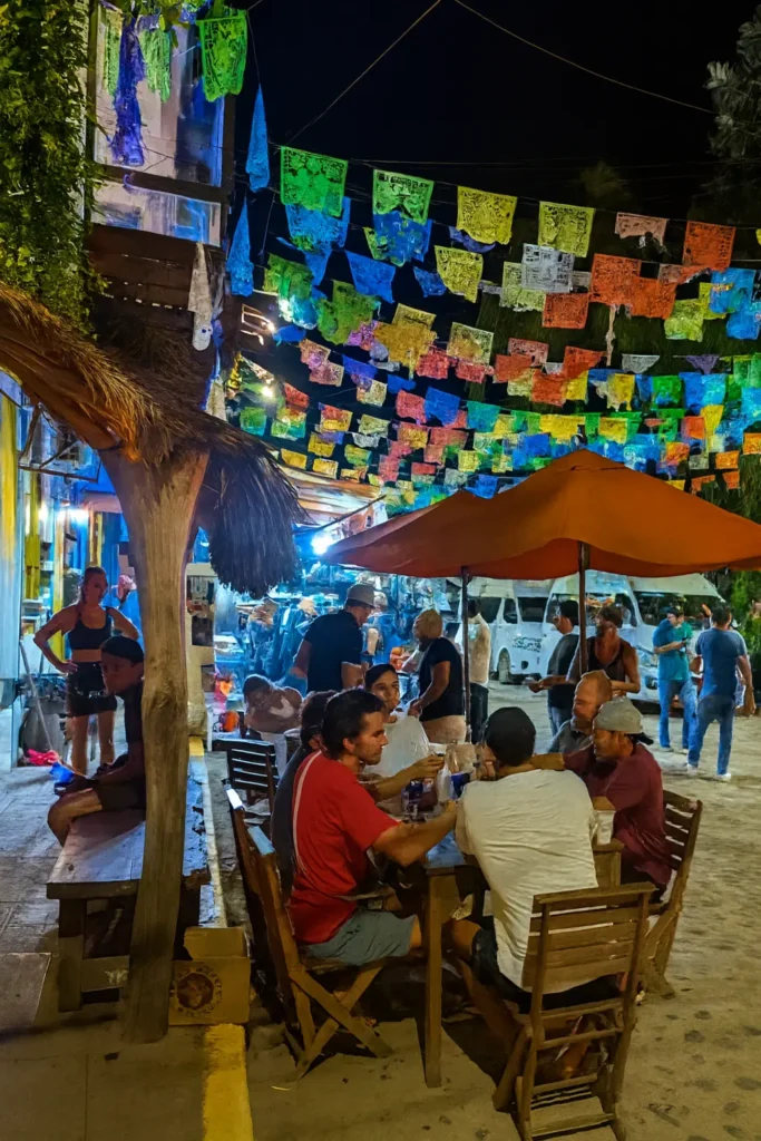 Lanterns, papel picado, and street music fill Sayulita’s evening air—a lively yet safe moment as travelers share dinner under the warm night lights.