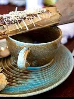 Una marquesita fresca descansa sobre una taza de cerámica con café matutino, capturando un sencillo momento de desayuno y la relajada cultura de cafés costeros.