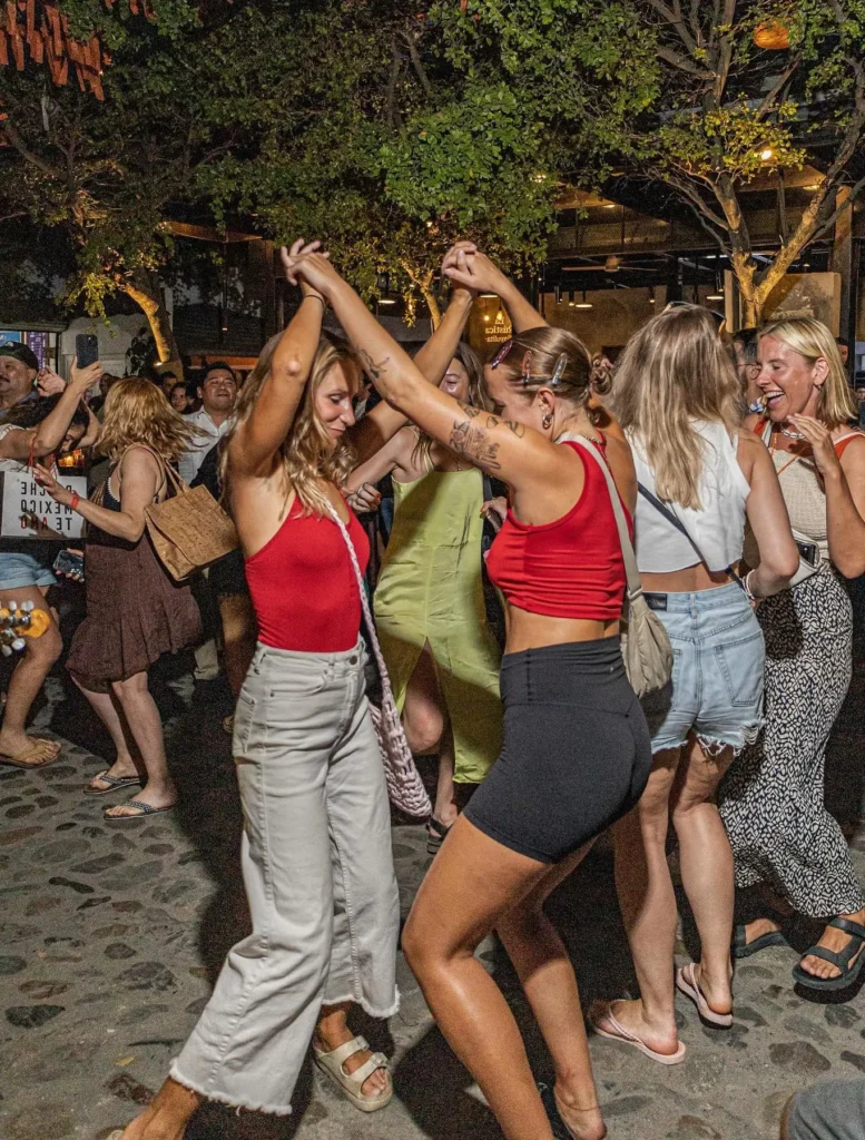 Friends dance on a lively street surrounded by music, crowds, and lights, capturing the vibrant Sayulita nightlife scene near restaurants and bars.