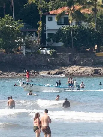 A beach-launched panga moves through the waves as travelers enjoy the shoreline, demonstrating how fishing in Sayulita starts directly from the sand.