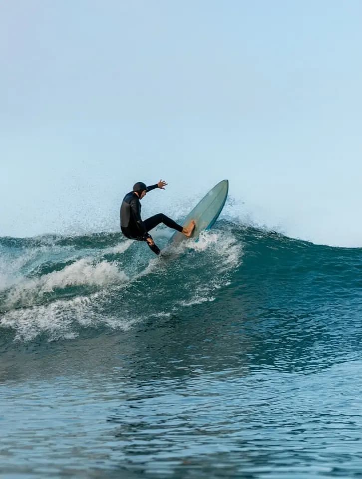 Surfer riding a wave, representing a laid-back beach lifestyle near cafés, bars, seafood stands, and restaurants offering casual food and drinks.