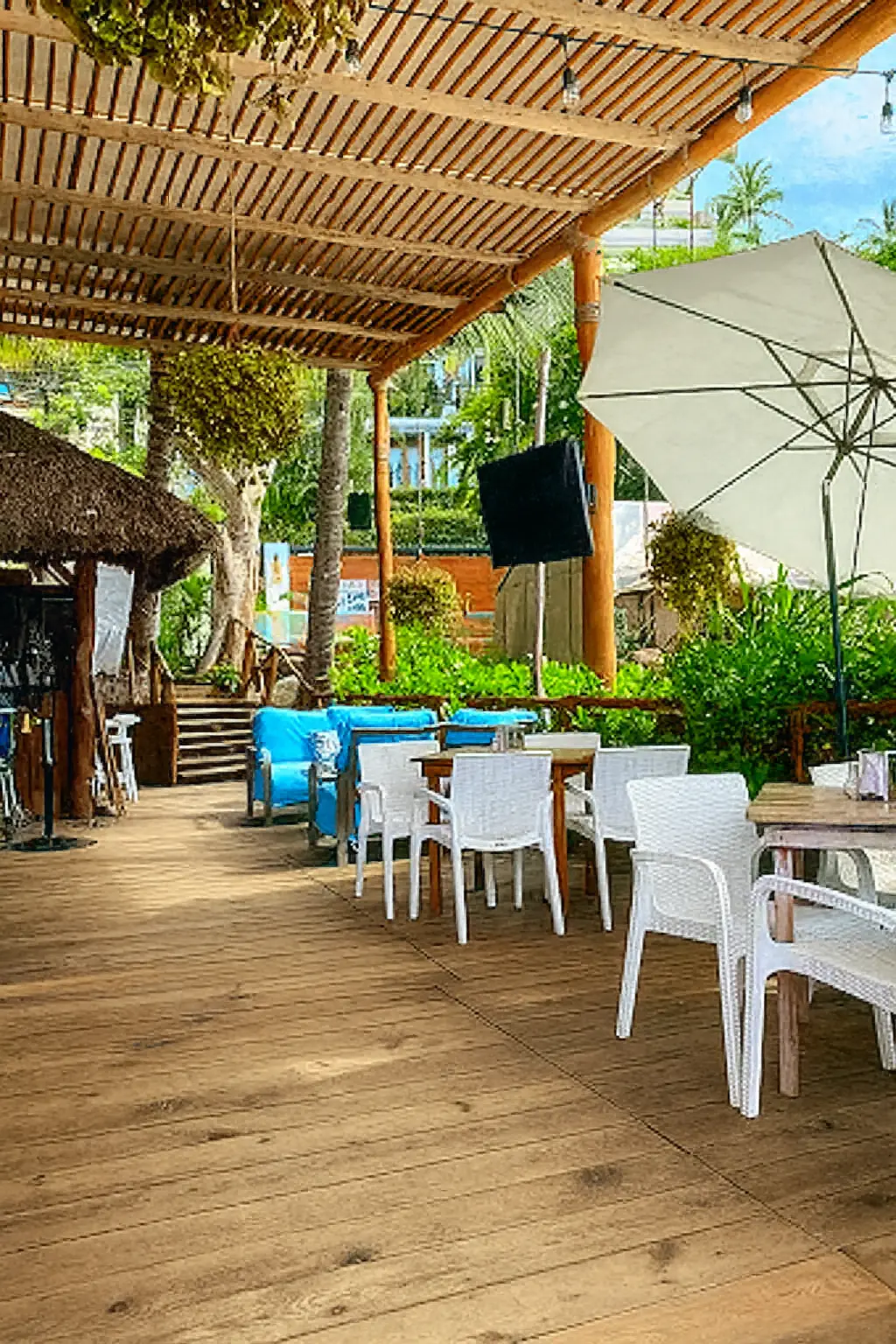 La sombra de palmeras y asientos acolchonados crean un espacio fresco para disfrutar sabores mediterráneos cerca del mar.