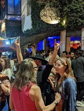 Crowded beer-garden street in Sayulita, with friends talking, loud music, and raised hands under colorful night lights in a festive, energetic scene.