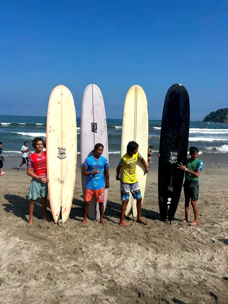 Surfers stand on sunlit sand as swells rise and fade, setting an easy backdrop for a relaxed, family-friendly shoreline retreat.